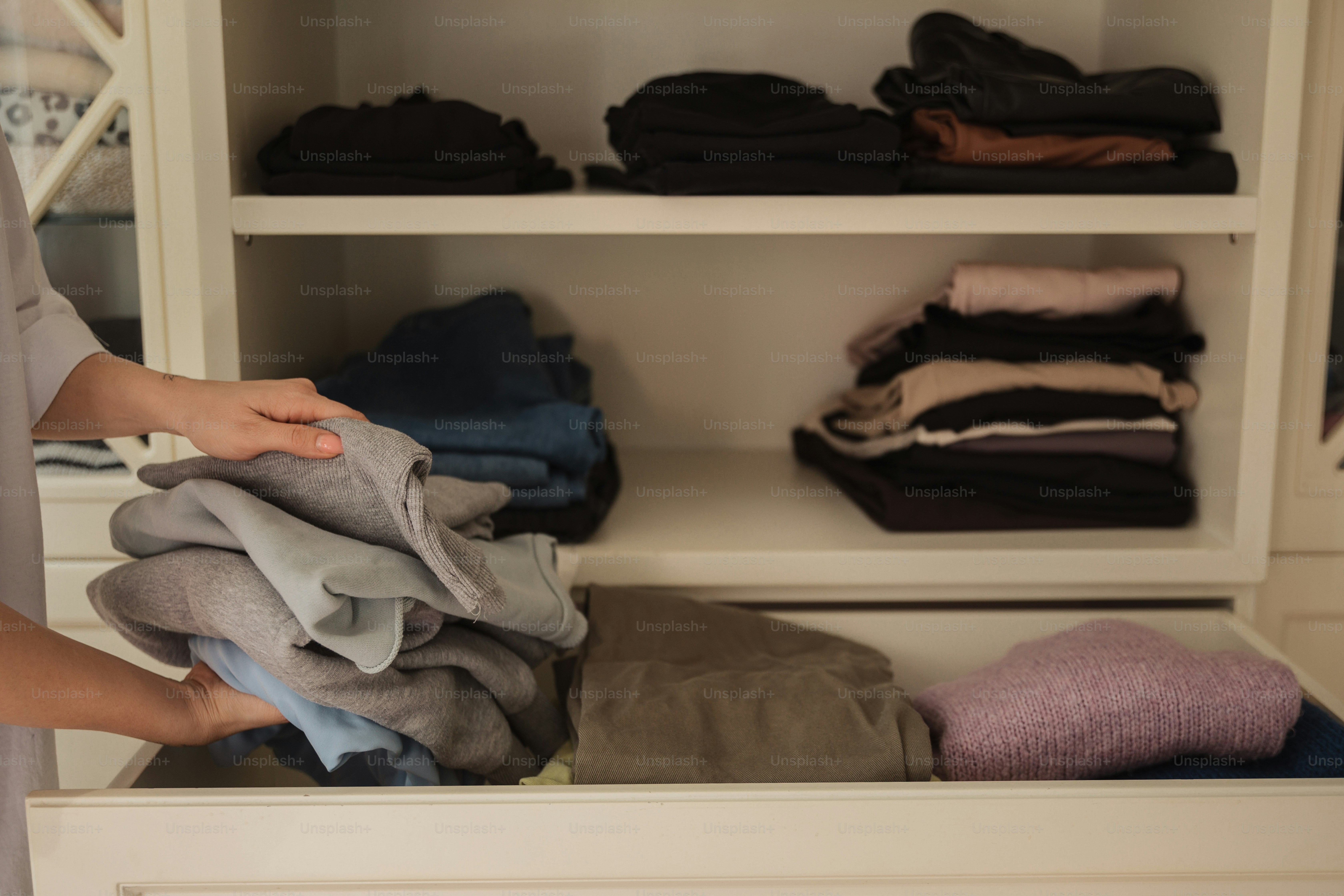 a person holding a pile of clothes in a closet