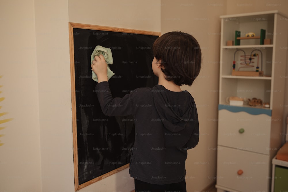 a young boy wiping up a chalkboard with a rag