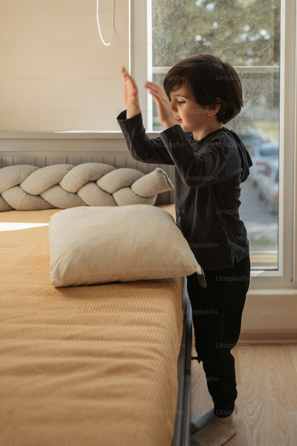 a little boy standing on top of a bed next to a window