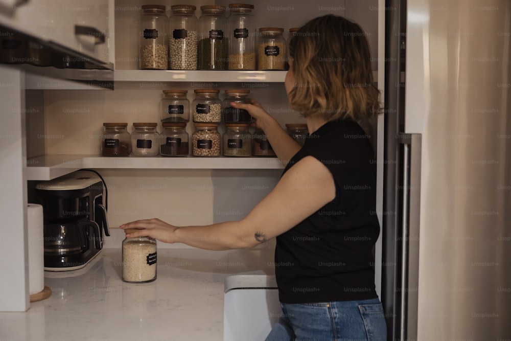 a woman reaching into a pantry filled with jars