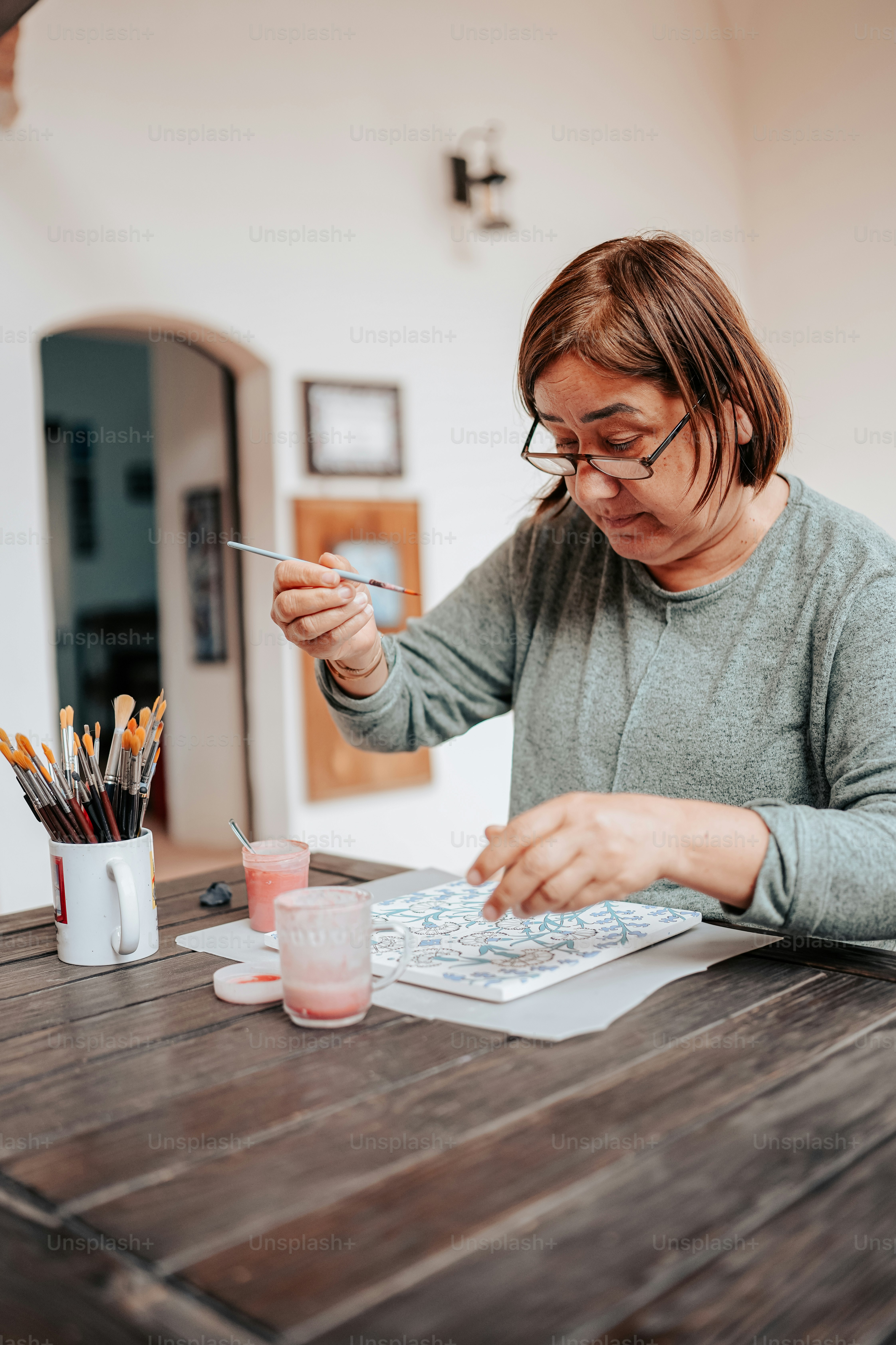 a woman sitting at a table with a book and paintbrush
