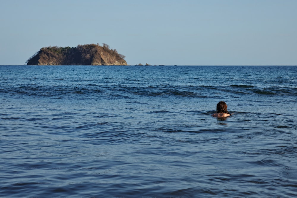 Una persona che nuota nell'oceano con una piccola isola sullo sfondo