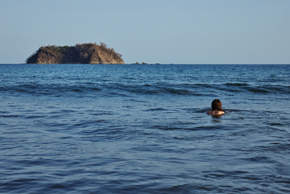 a person swimming in the ocean with a small island in the background