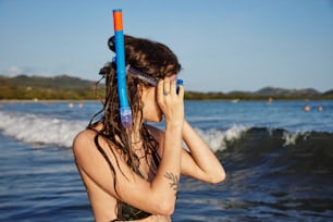 uma mulher em um biquíni segurando um par de snorkels para seu rosto