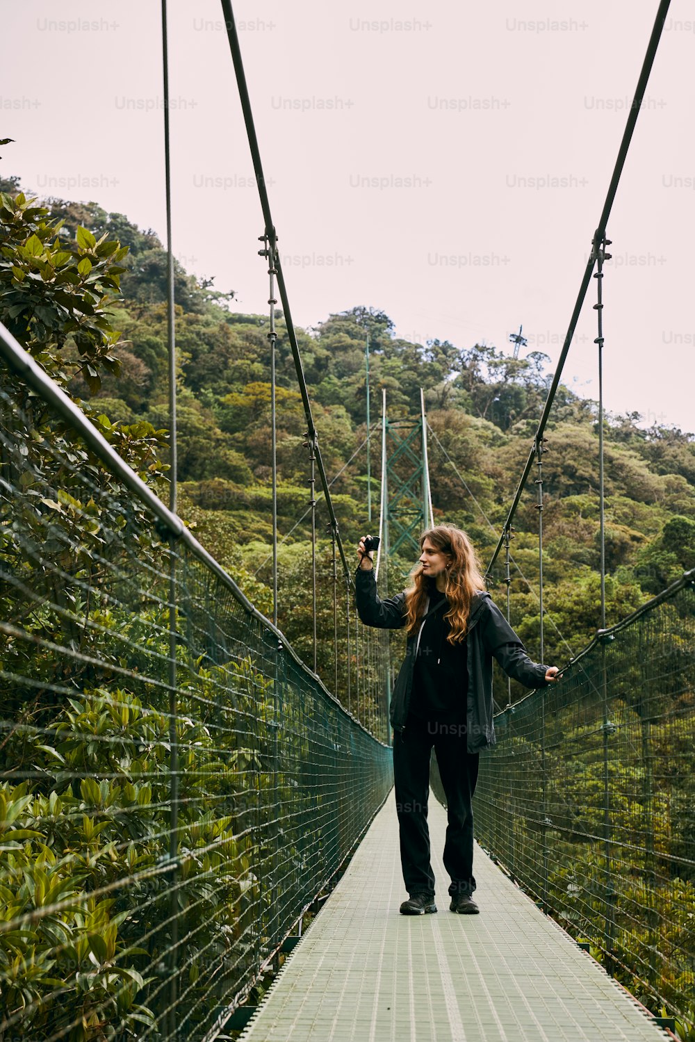 a woman is walking across a suspension bridge