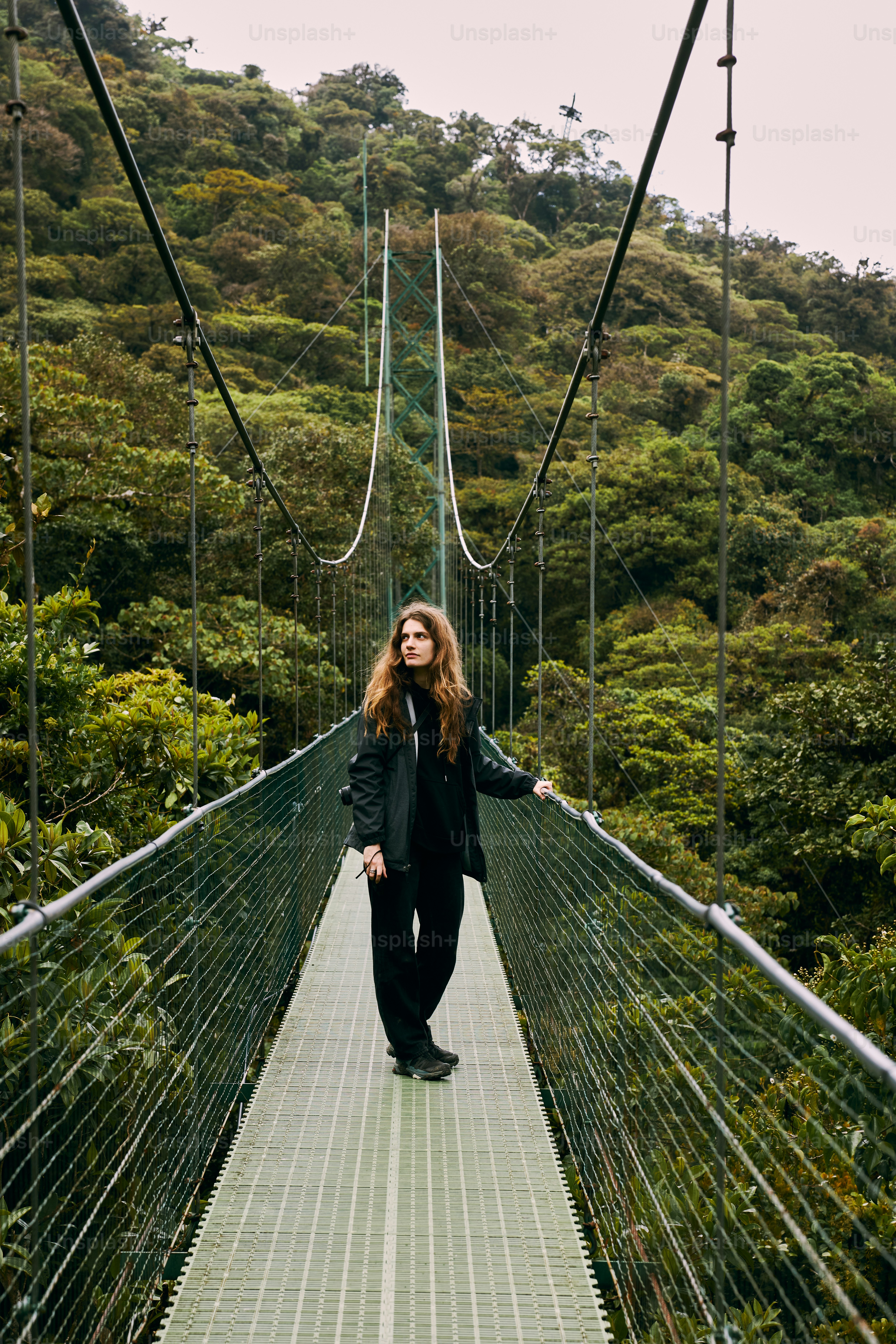 a woman standing on a suspension bridge in the middle of a forest