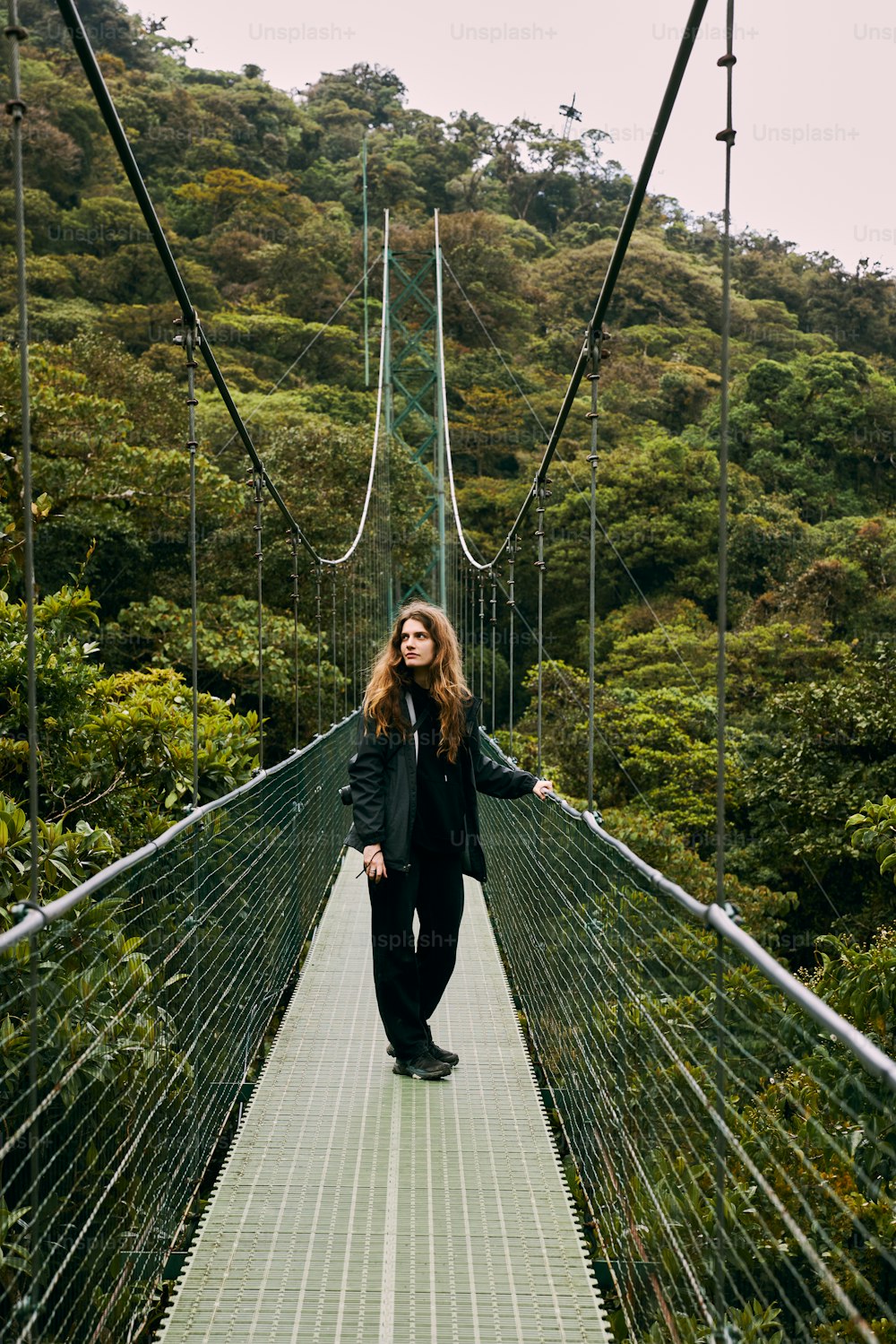 a woman standing on a suspension bridge in the middle of a forest