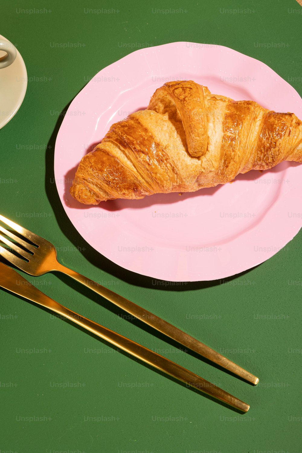 a croissant on a pink plate next to a fork