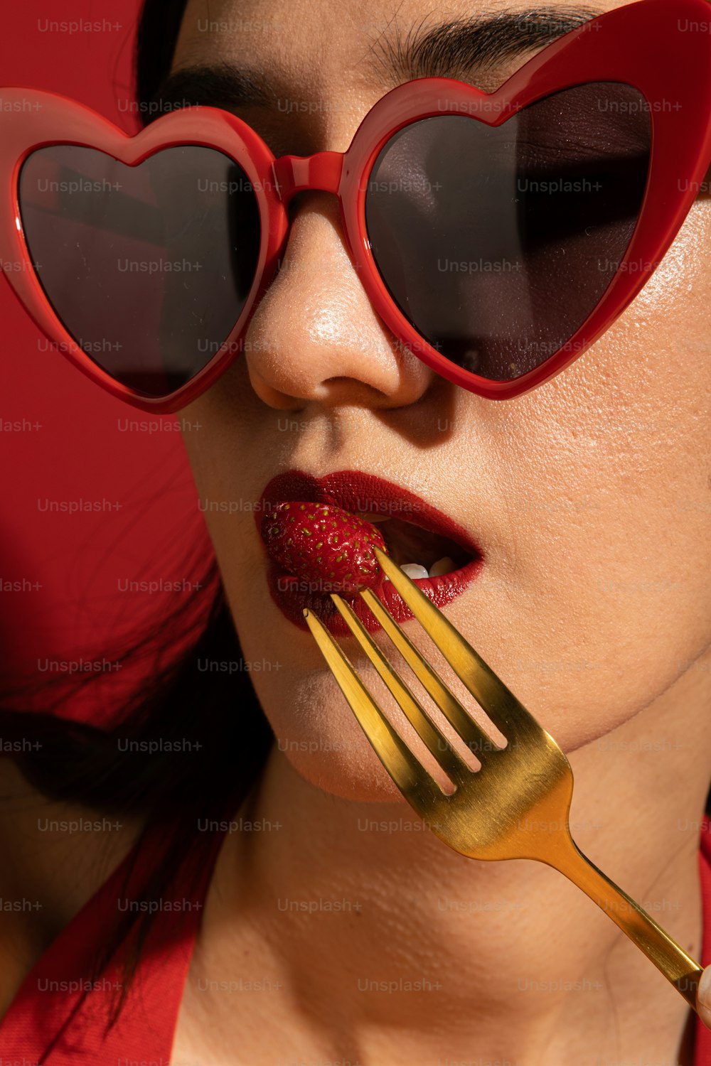 uma mulher com óculos em forma de coração e um garfo na boca