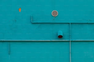 a blue wall with pipes and a vent on it