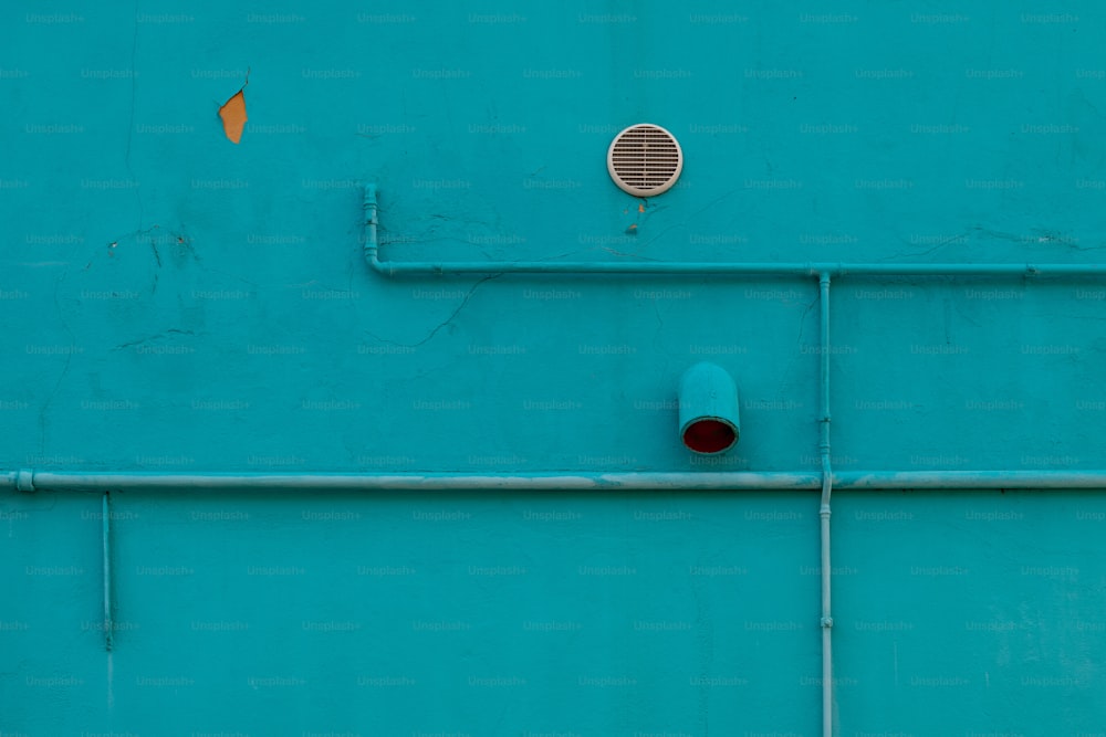 a blue wall with pipes and a vent on it