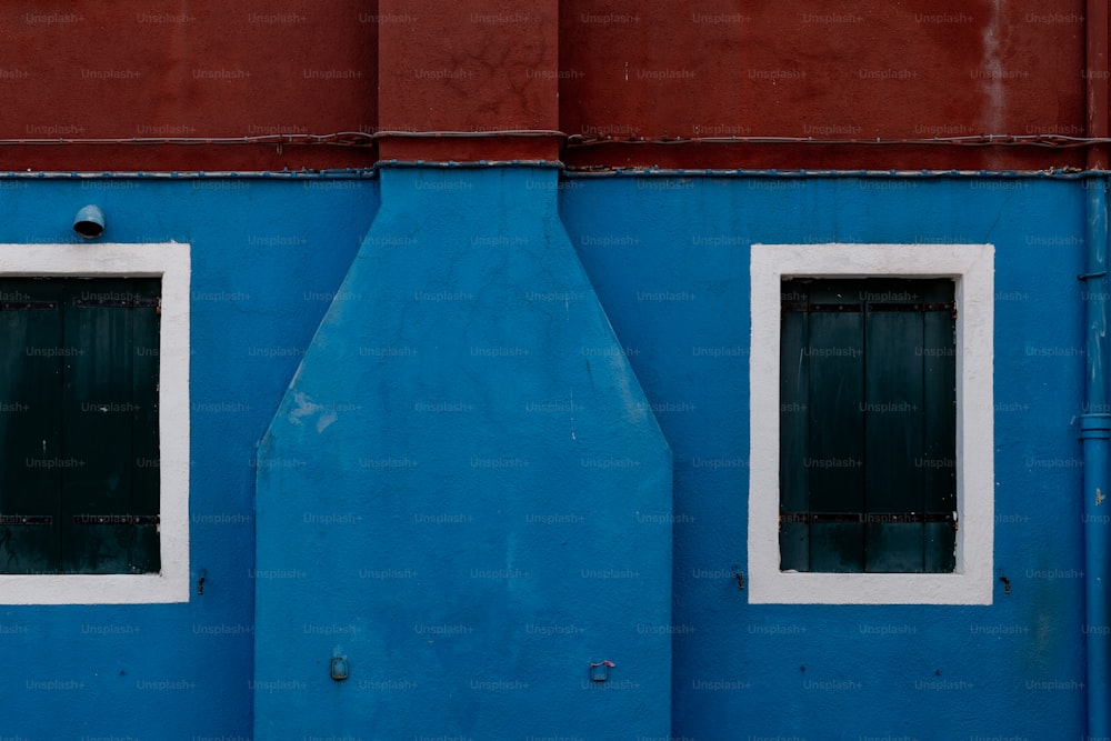 a blue building with two windows and a red wall