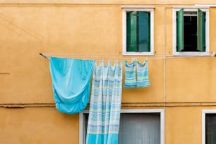 a yellow building with two windows and a blue curtain