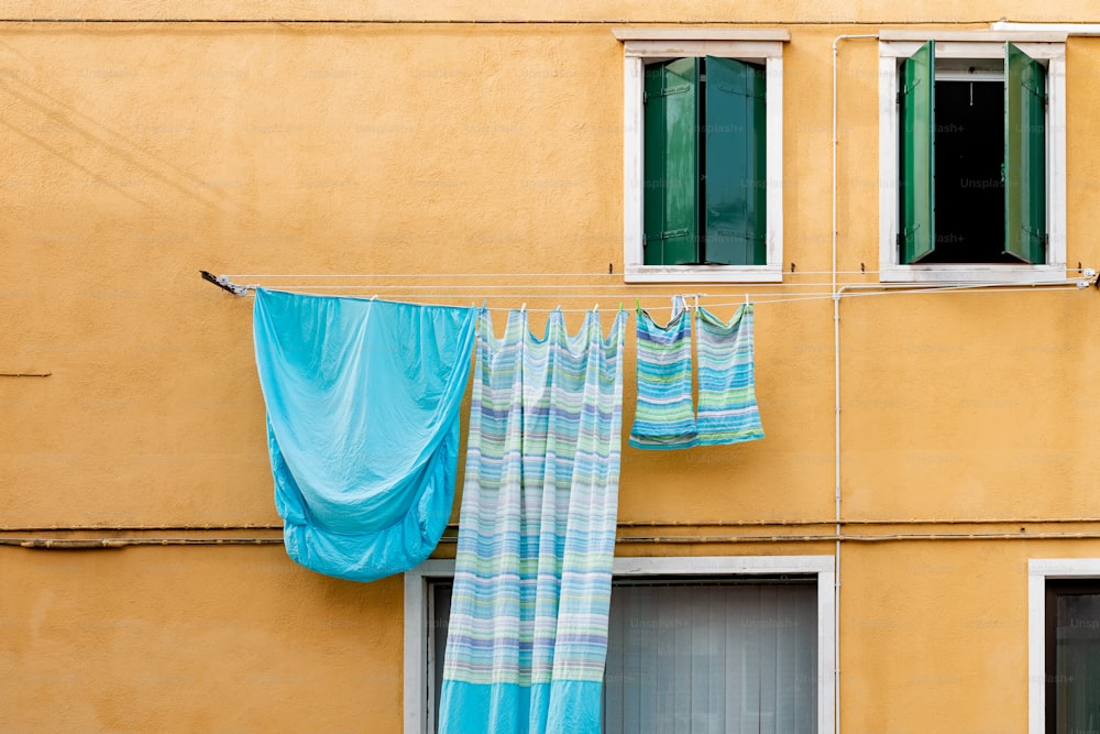 a yellow building with two windows and a blue curtain