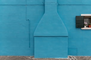 a blue building with a window and a vase with flowers