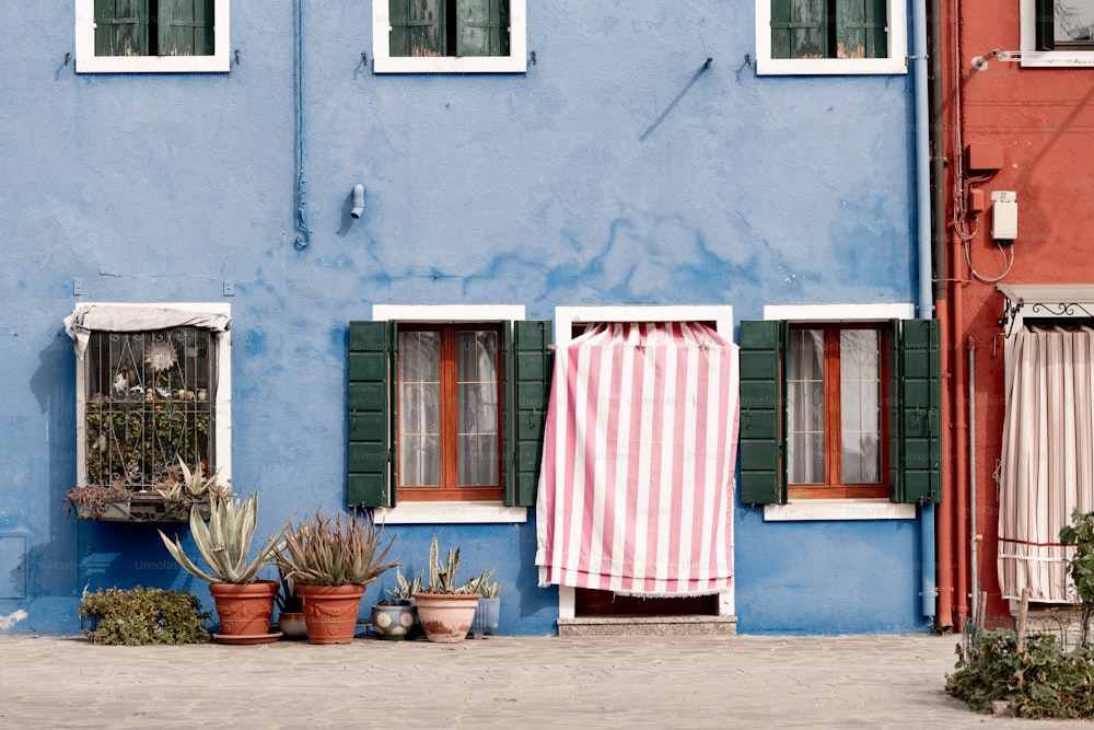 a blue building with green shutters and a striped towel hanging out of the window