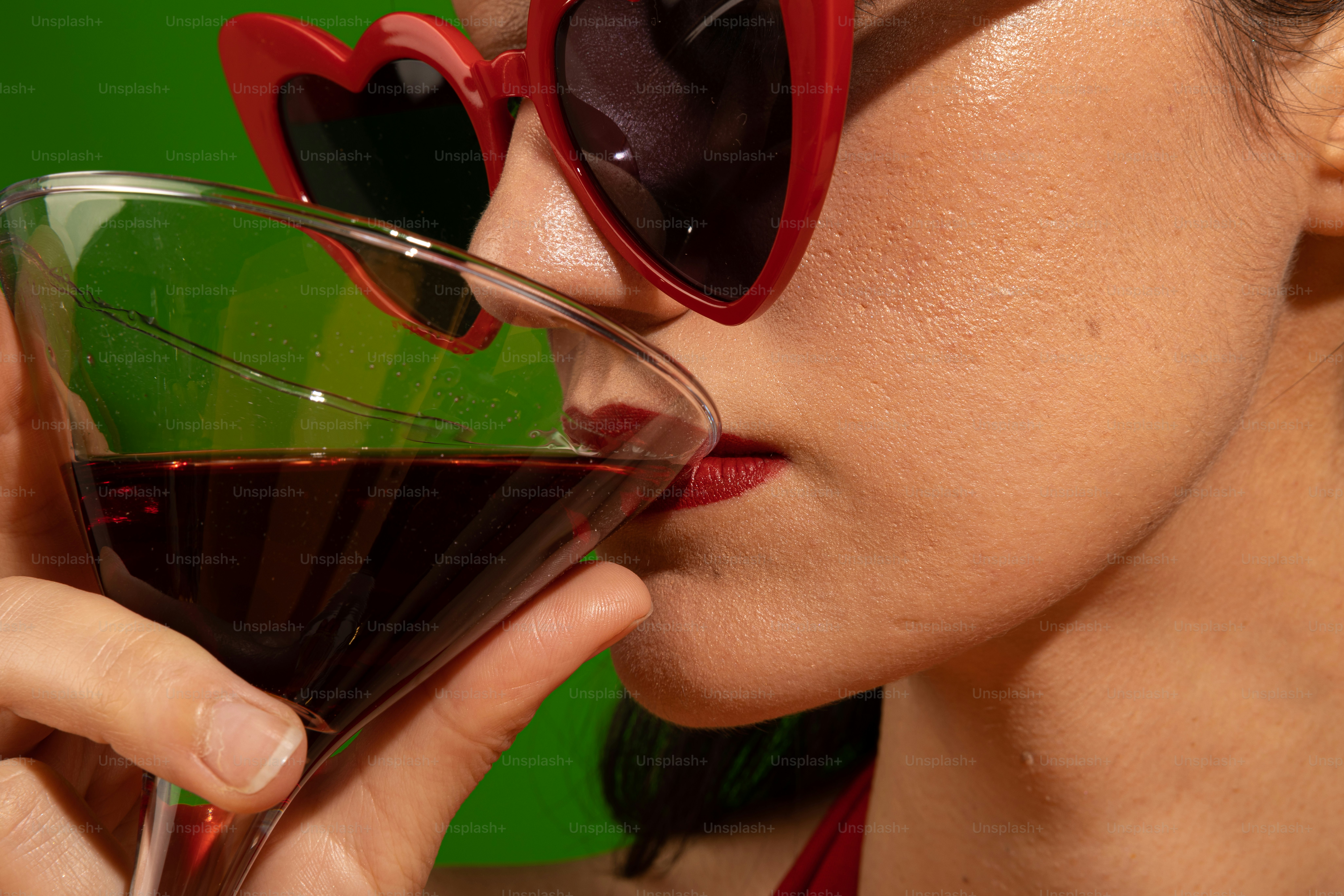 빨간 선글라스를 쓴 여자가 와인 한 잔을 마시고 있다