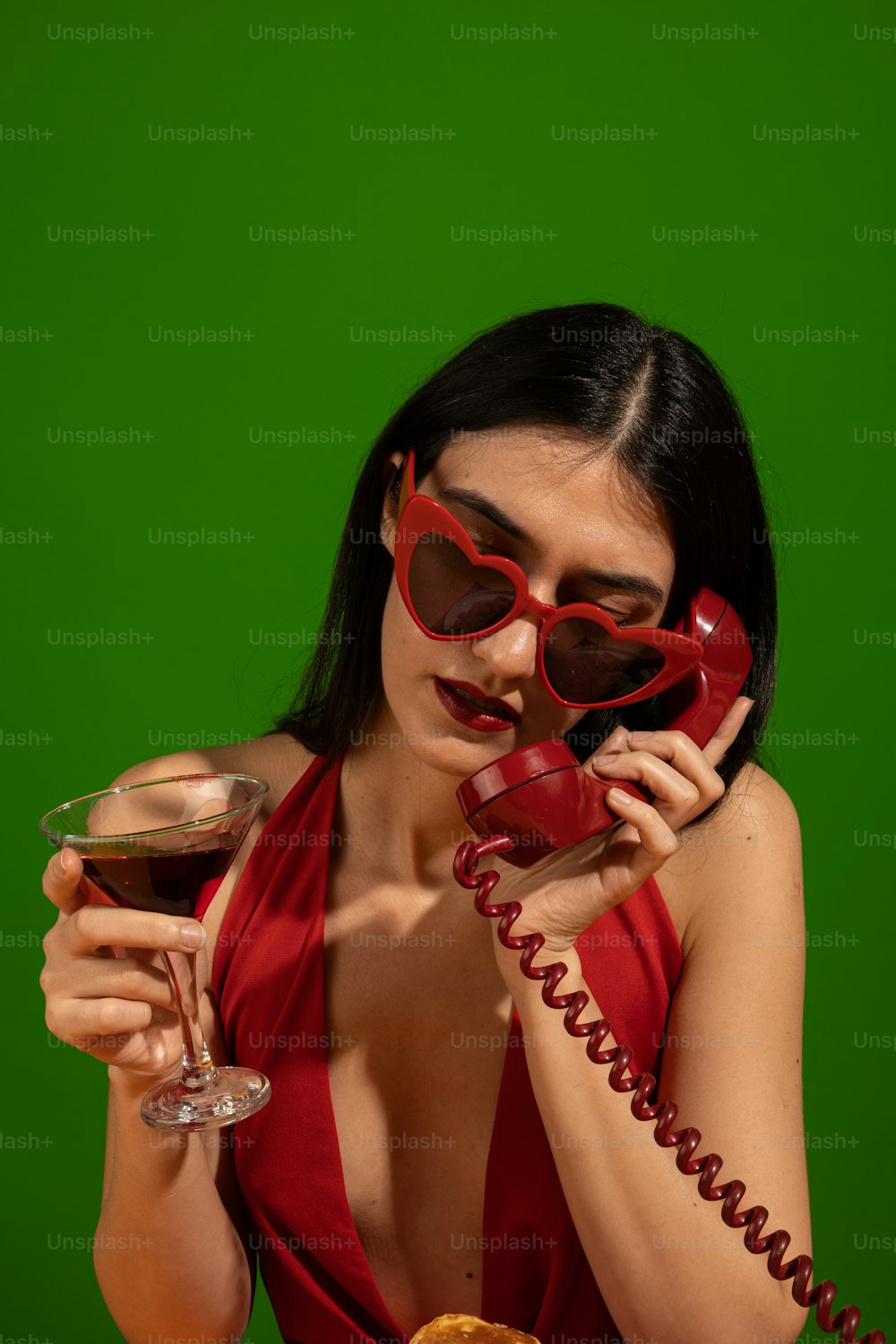 a woman in a red dress holding a glass of wine and talking on the phone