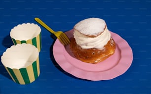 a pink plate topped with a pastry next to two cupcakes