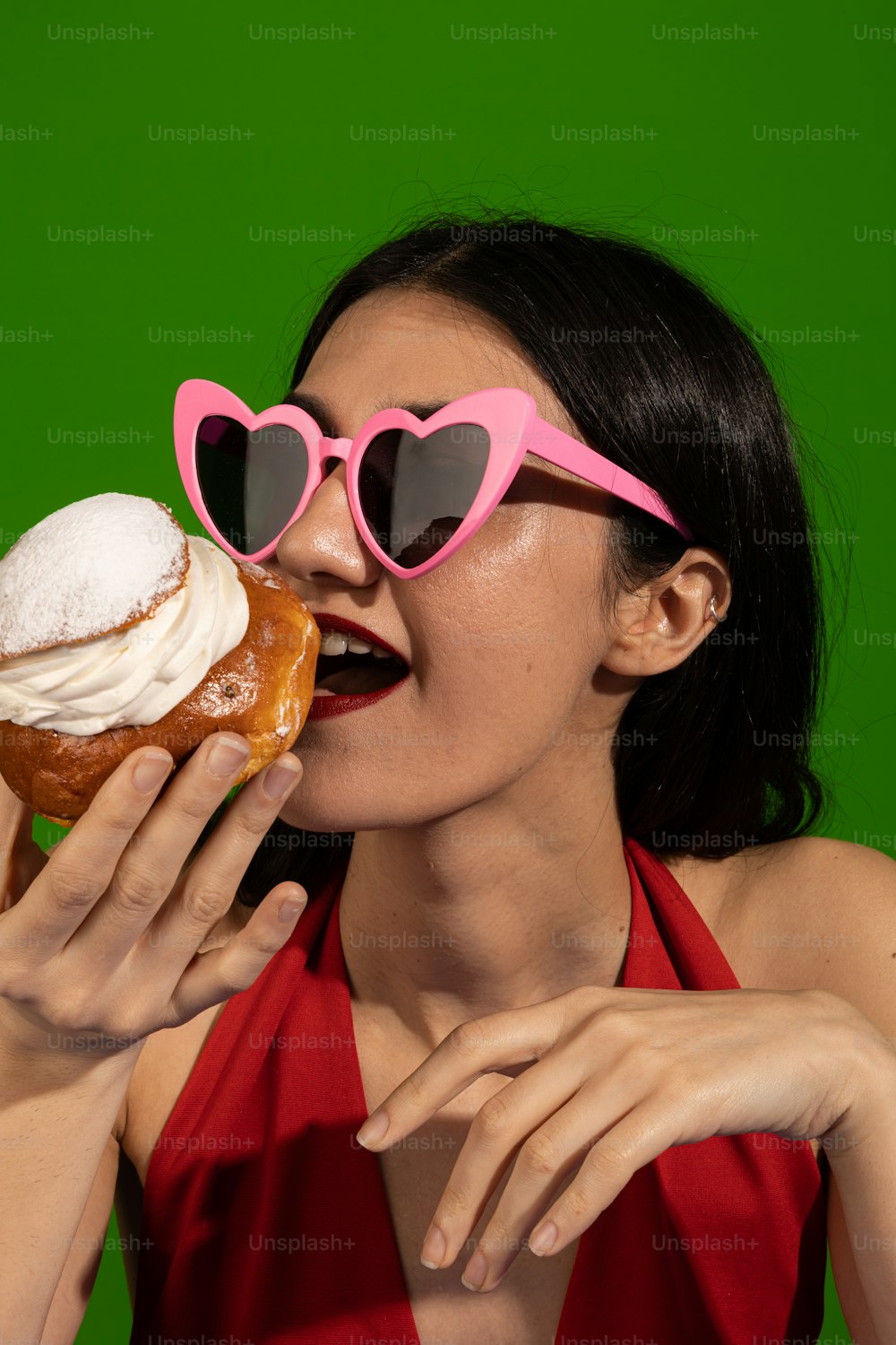 Una mujer con gafas de sol en forma de corazón comiendo una rosquilla