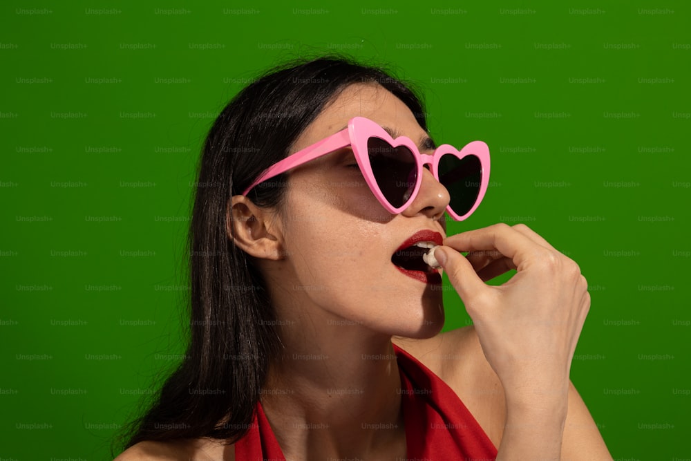 Una donna che indossa occhiali da sole rosa a forma di cuore su uno sfondo verde