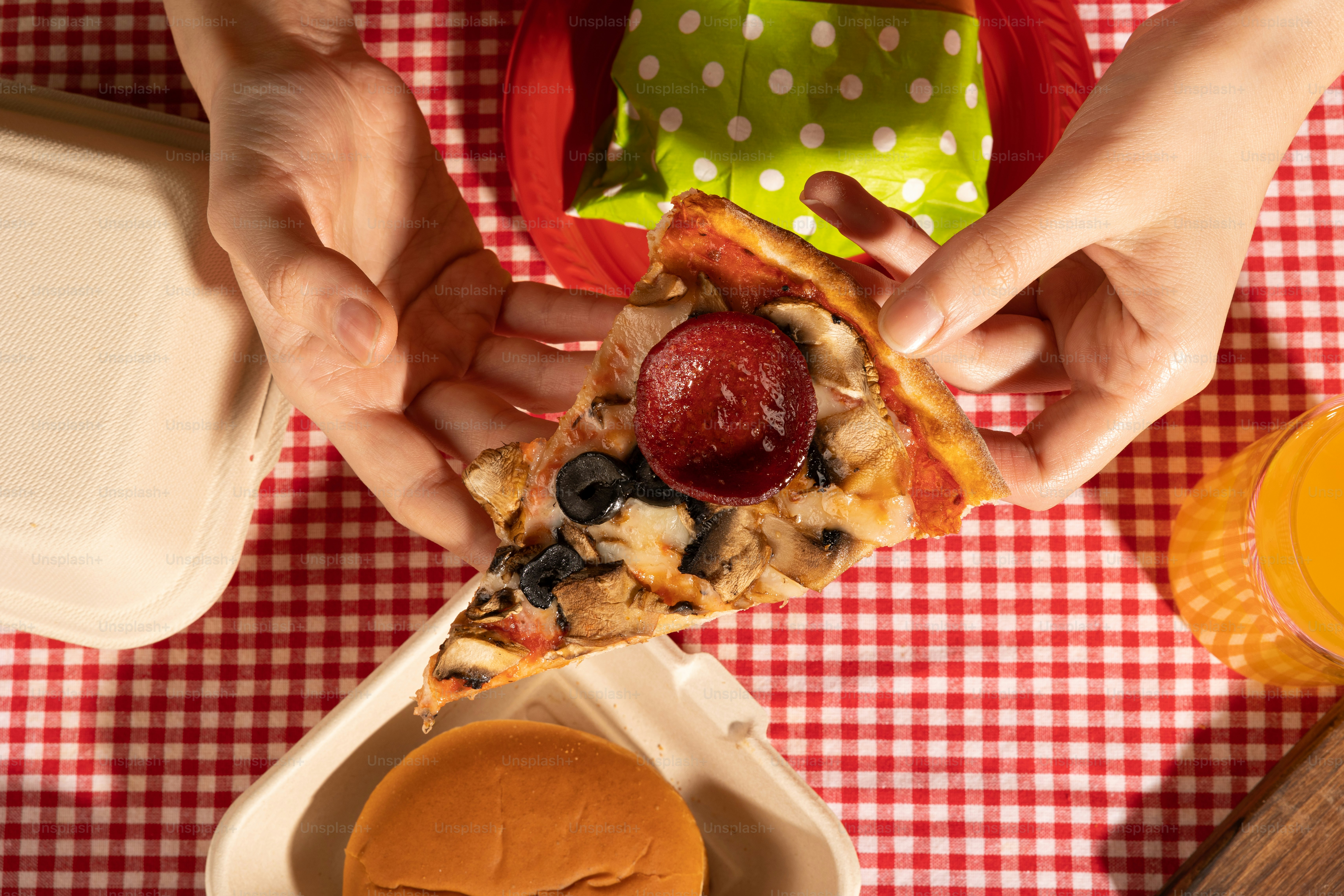 빨간색과 흰색 체크 무늬 식탁보에 피자 한 조각을 먹는 사람
