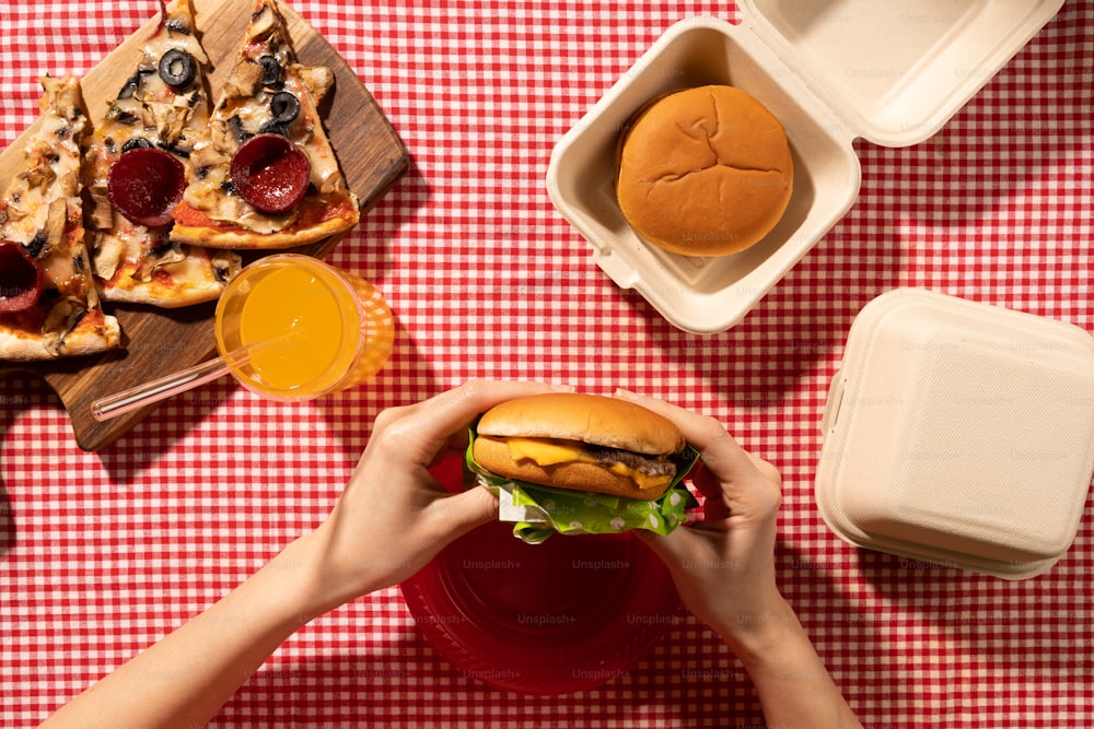 a person holding a hamburger in front of a table full of food