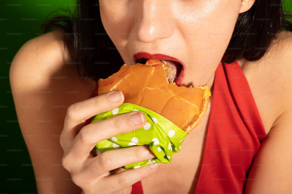 Une femme en haut rouge mangeant un sandwich