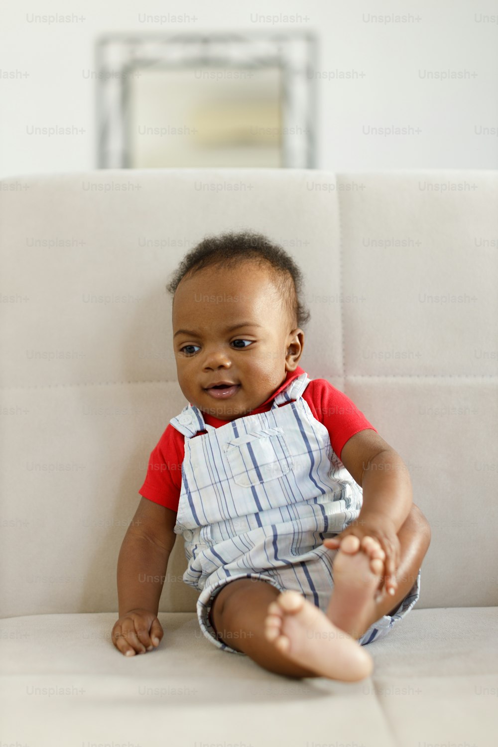 um bebê sentado em um sofá branco com uma camisa vermelha