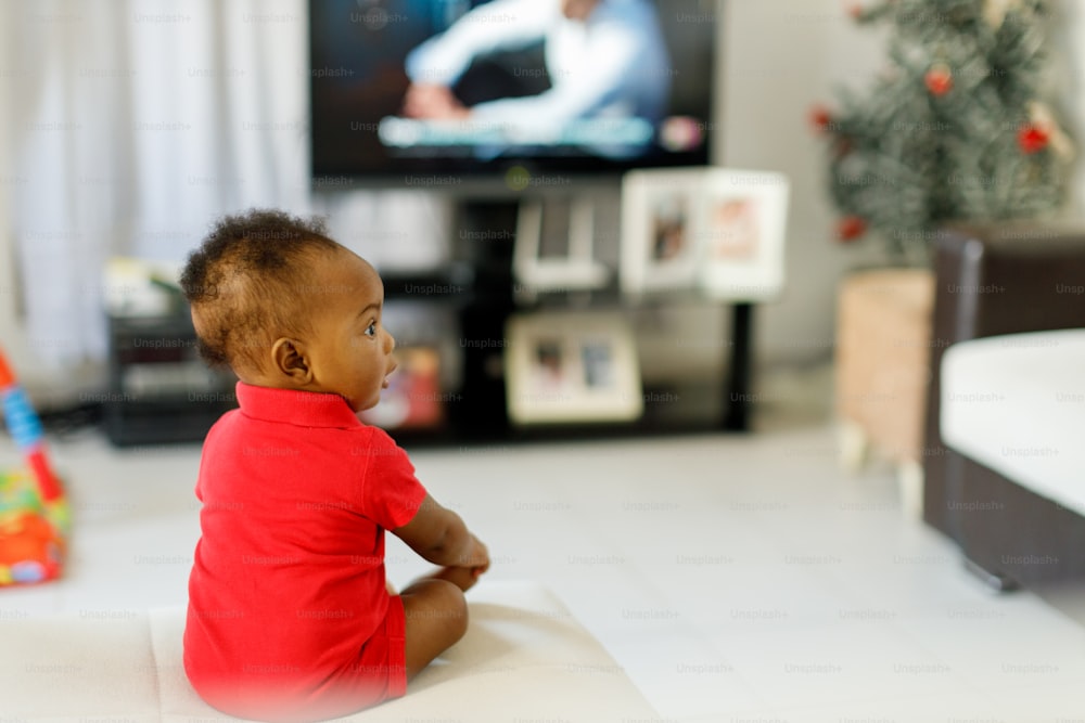 um bebê sentado no chão em frente a uma tv