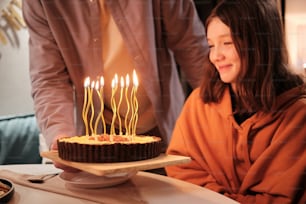 a woman sitting in front of a cake with lit candles