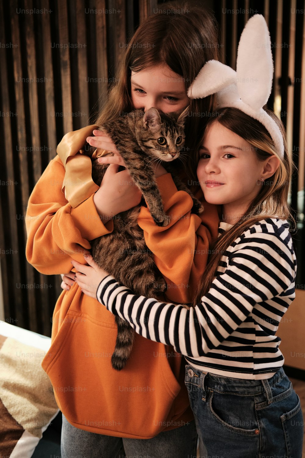 Zwei Mädchen in Hasenohren umarmen eine Katze