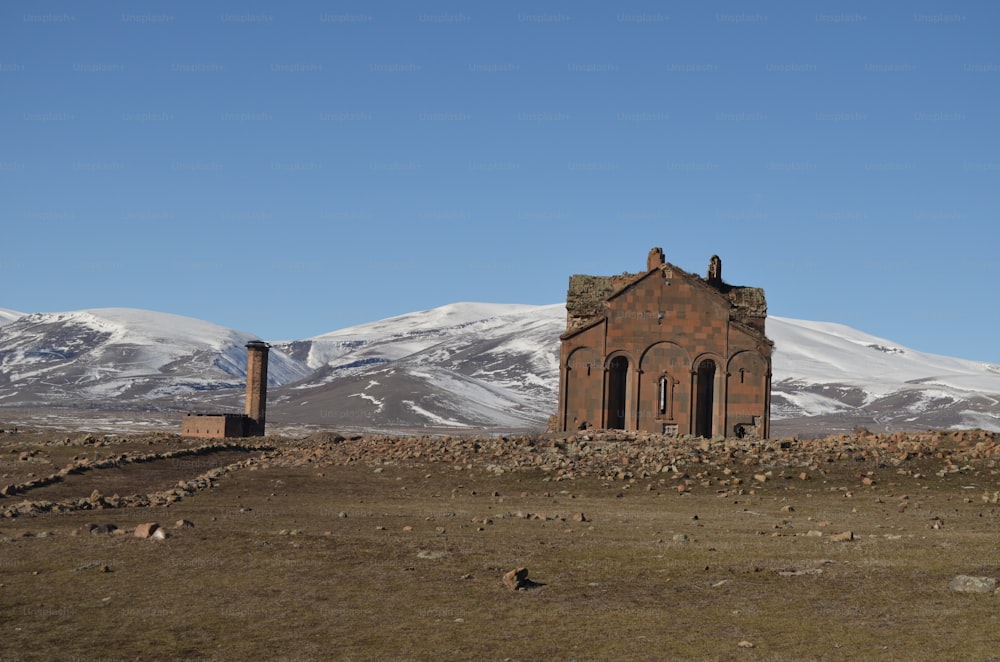 an old building in a field with mountains in the background