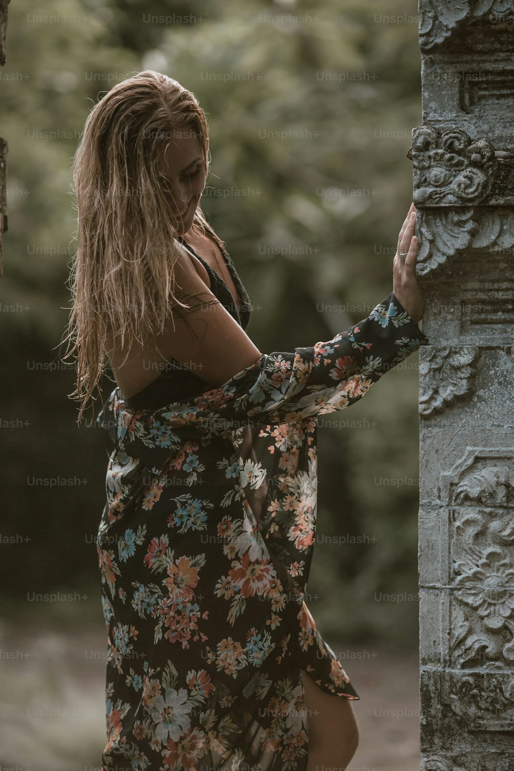 a woman in a floral dress leaning against a pillar