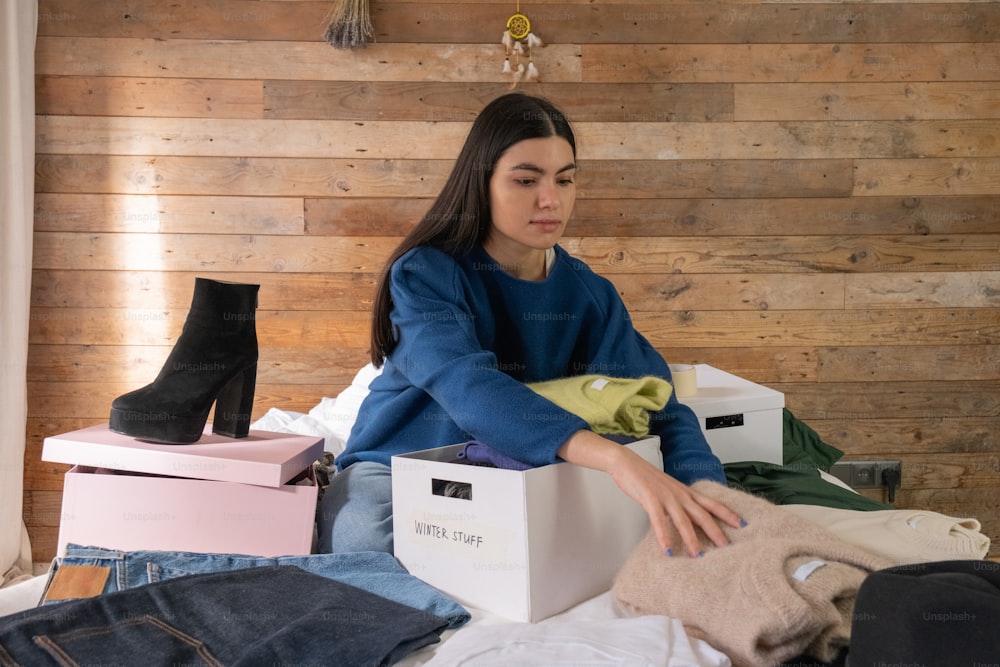 a woman sitting on a bed with a box of clothes