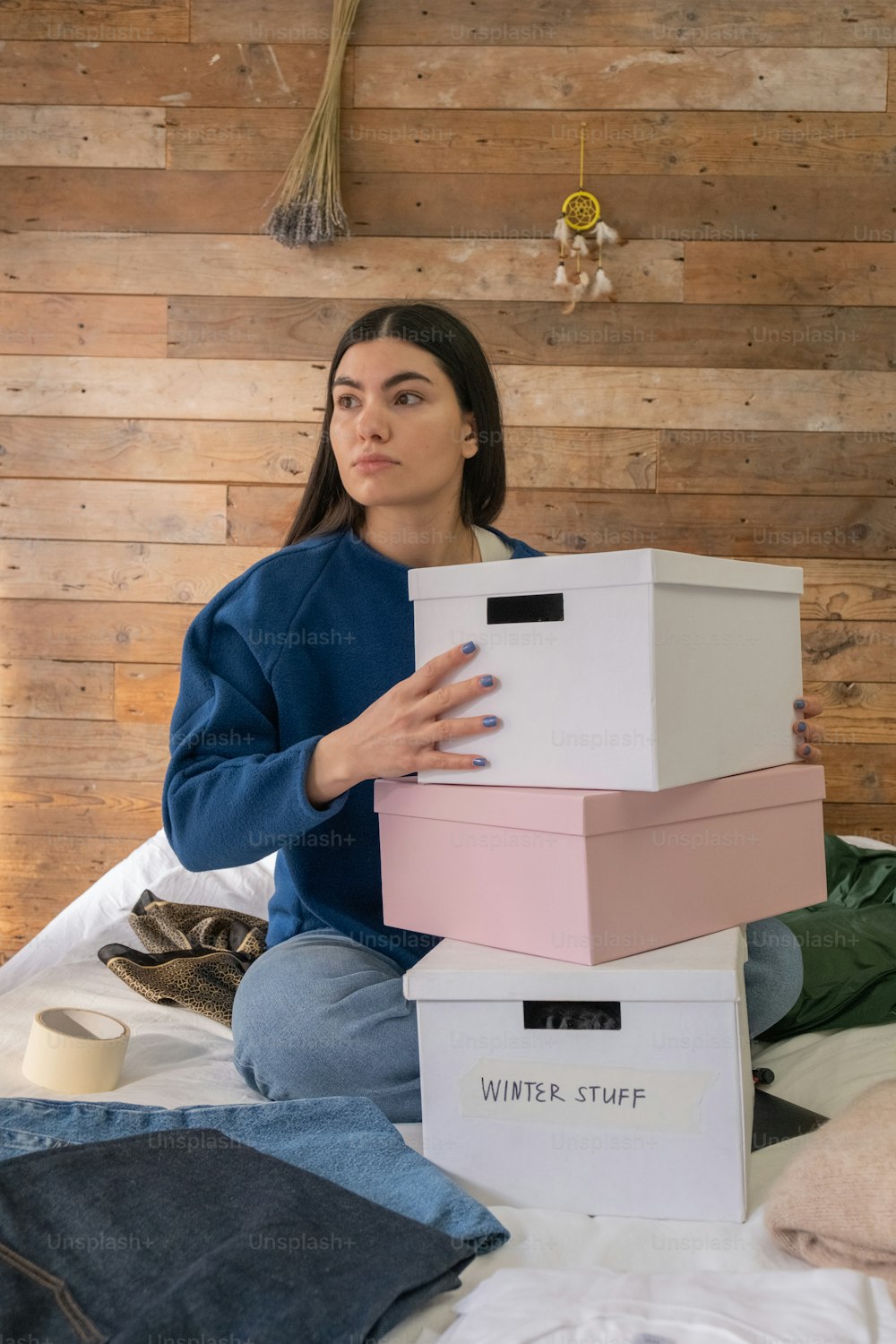 a woman sitting on a bed holding a stack of boxes