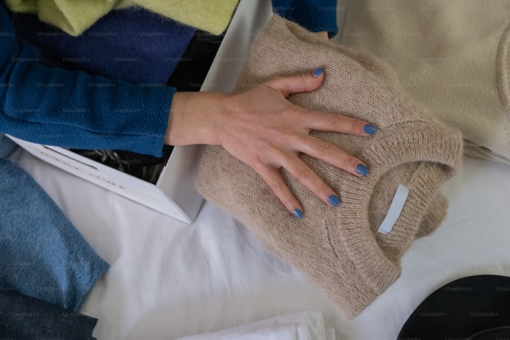 a woman's hands holding a sweater and a pair of jeans
