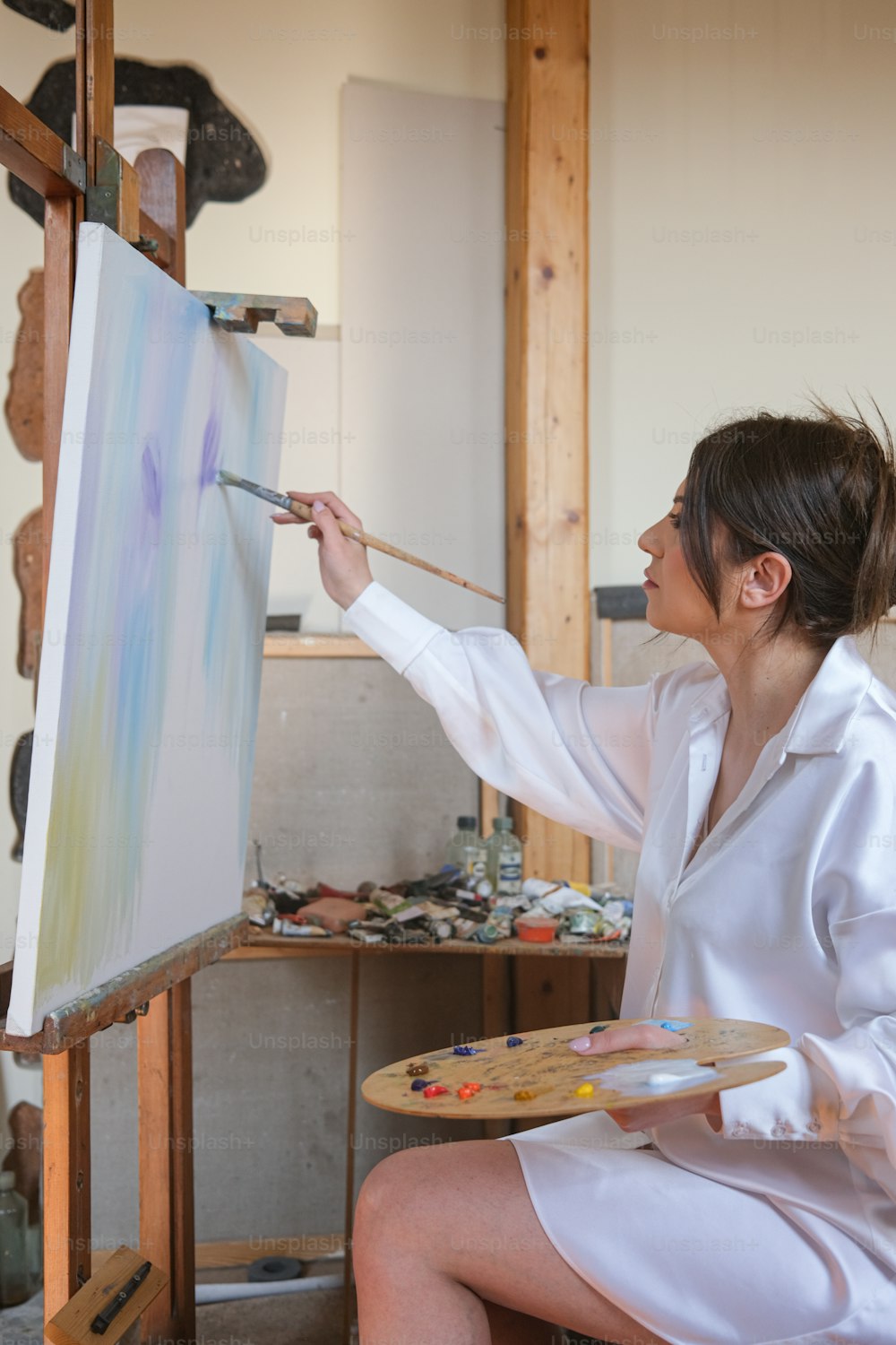 a woman in a white shirt is painting on a easel