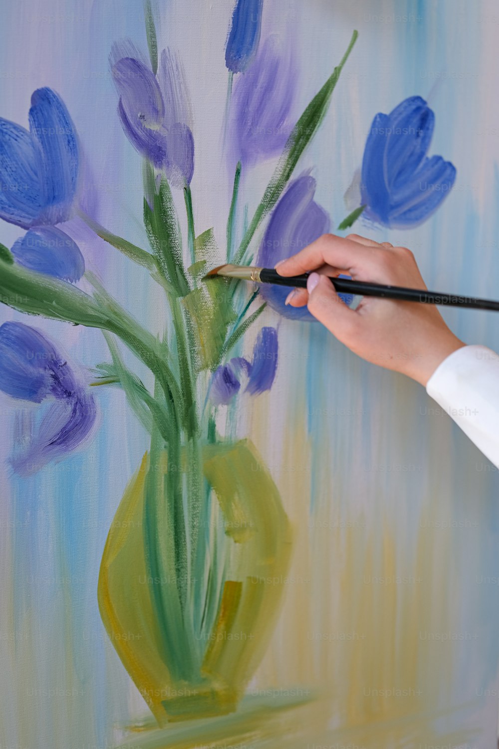 Una persona pintando un jarrón con flores púrpuras