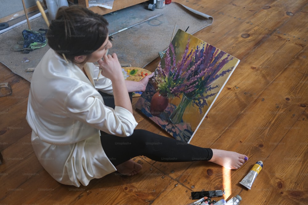 una donna seduta sul pavimento accanto a un dipinto