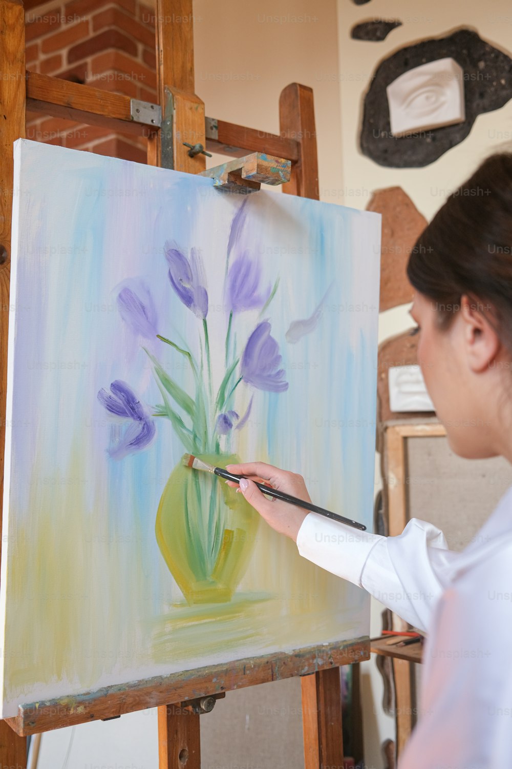 Une femme peint un vase avec des fleurs violettes