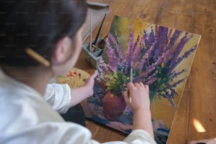 a woman is painting a vase with flowers