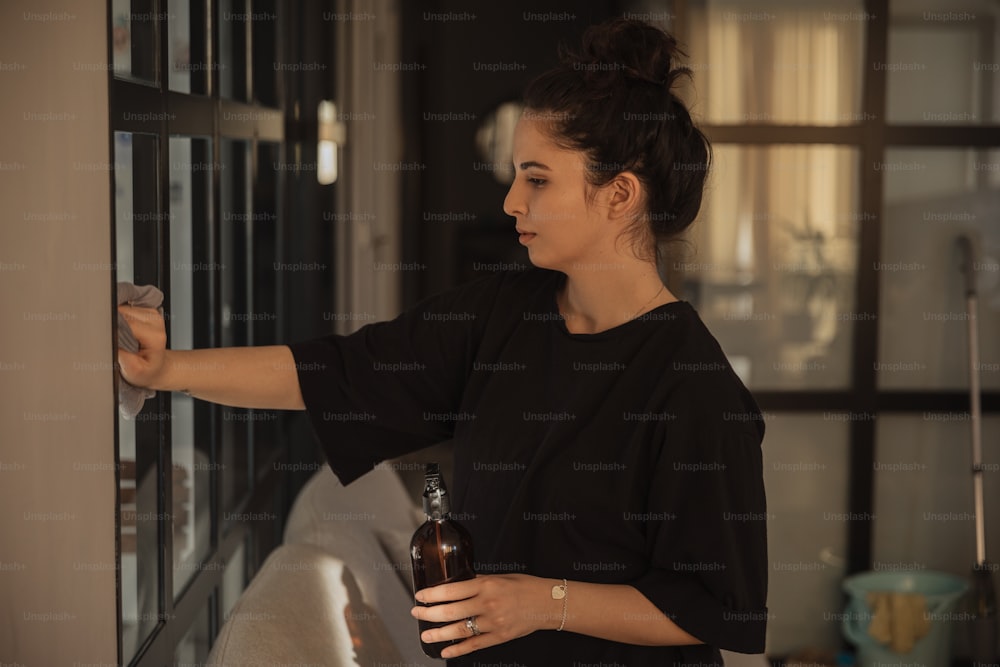 Una mujer abriendo una ventana con una botella de cerveza