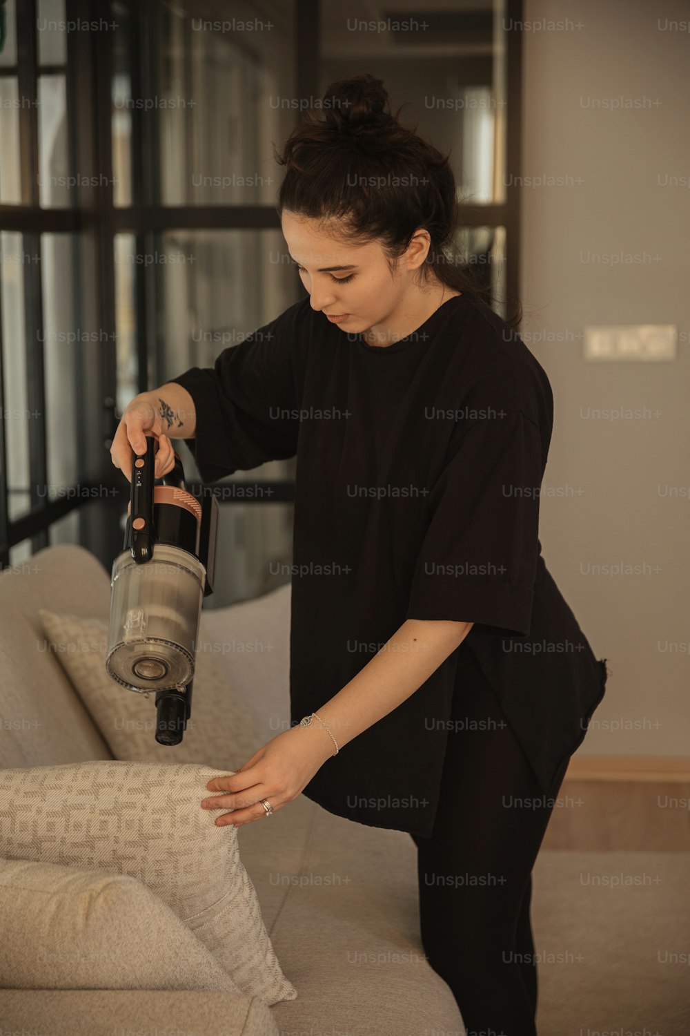 Une femme en chemise noire utilisant un aspirateur sur un canapé