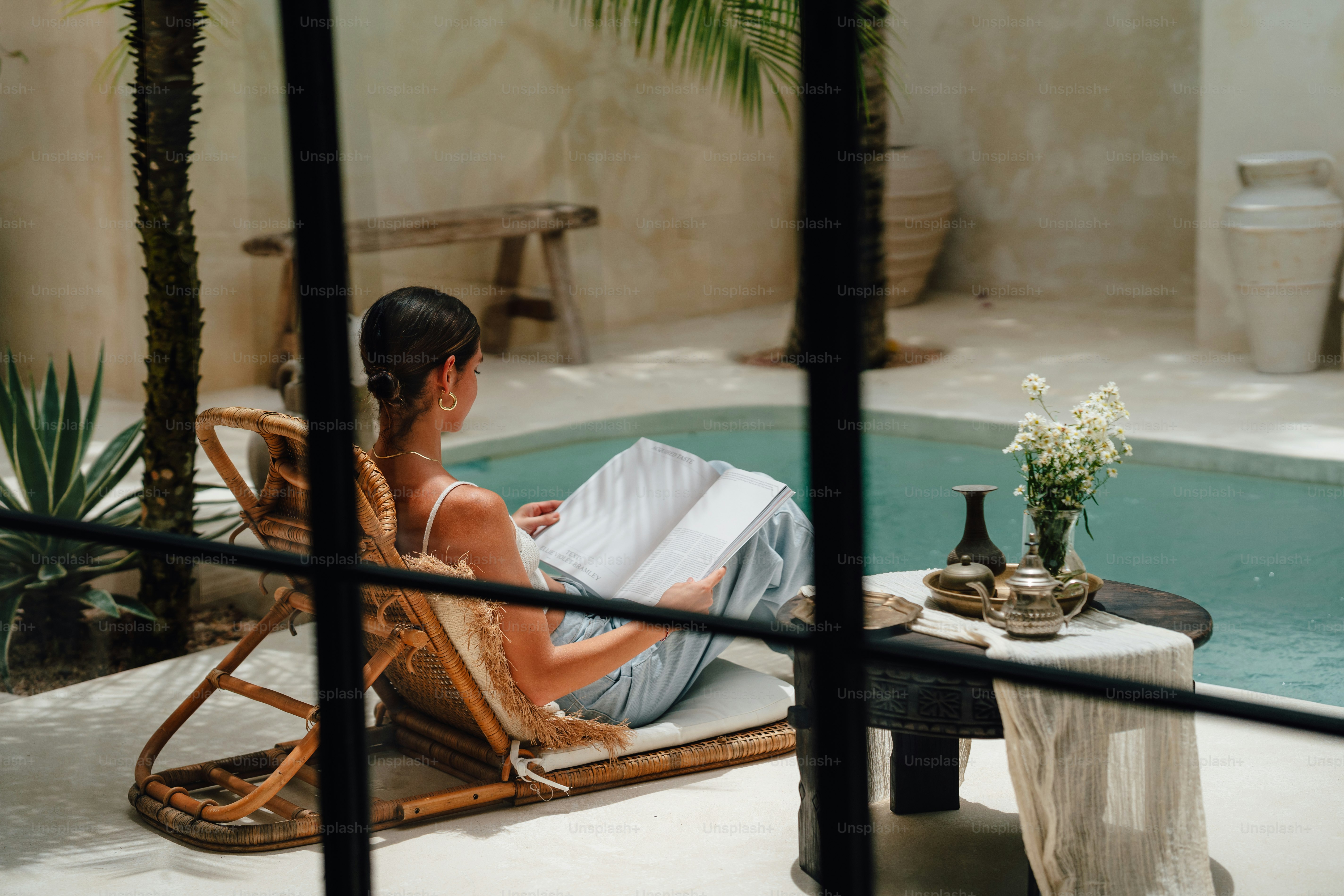 a woman sitting in a chair by a pool reading a book