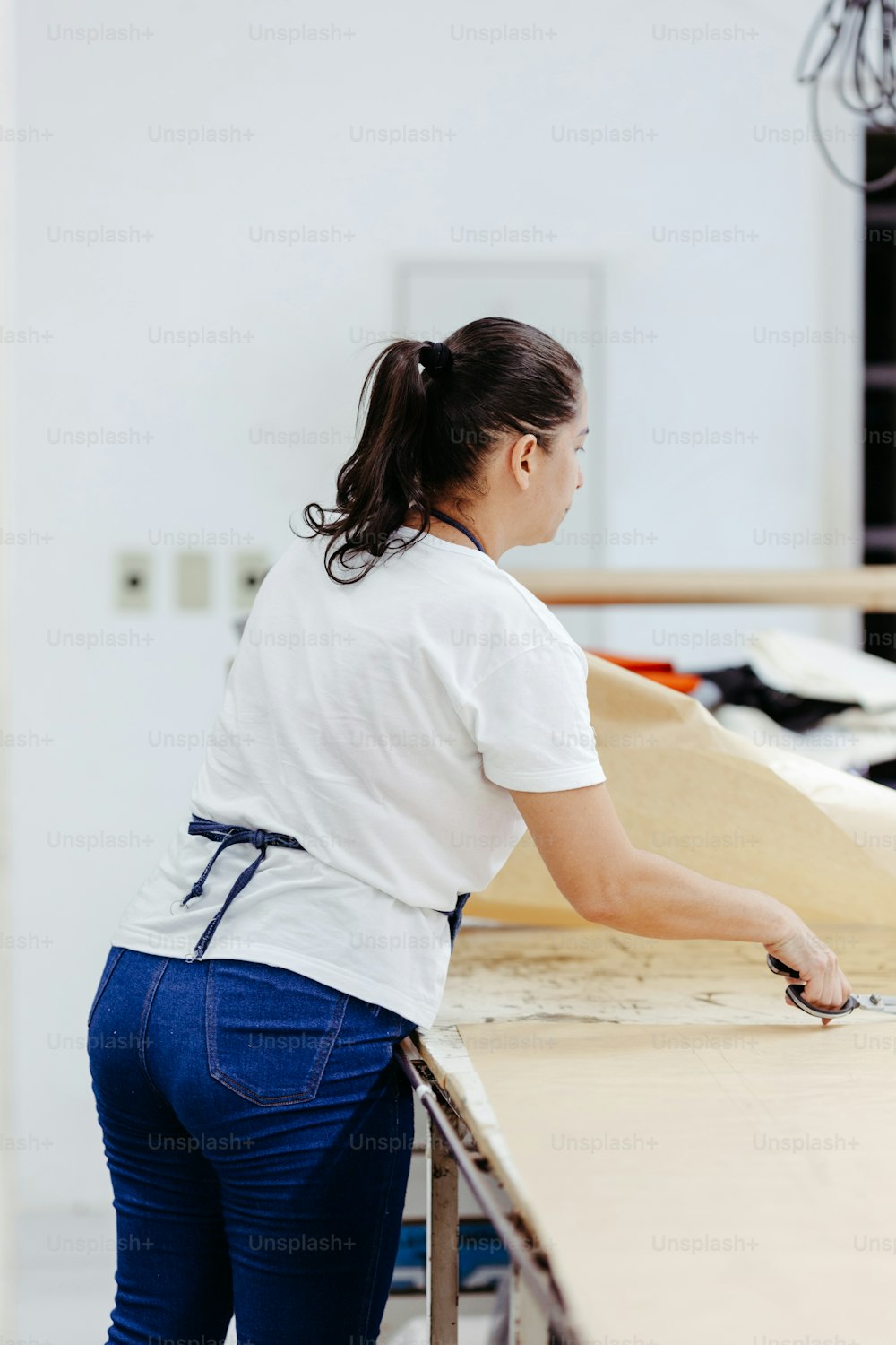 a woman in a white shirt and blue jeans working on a piece of wood