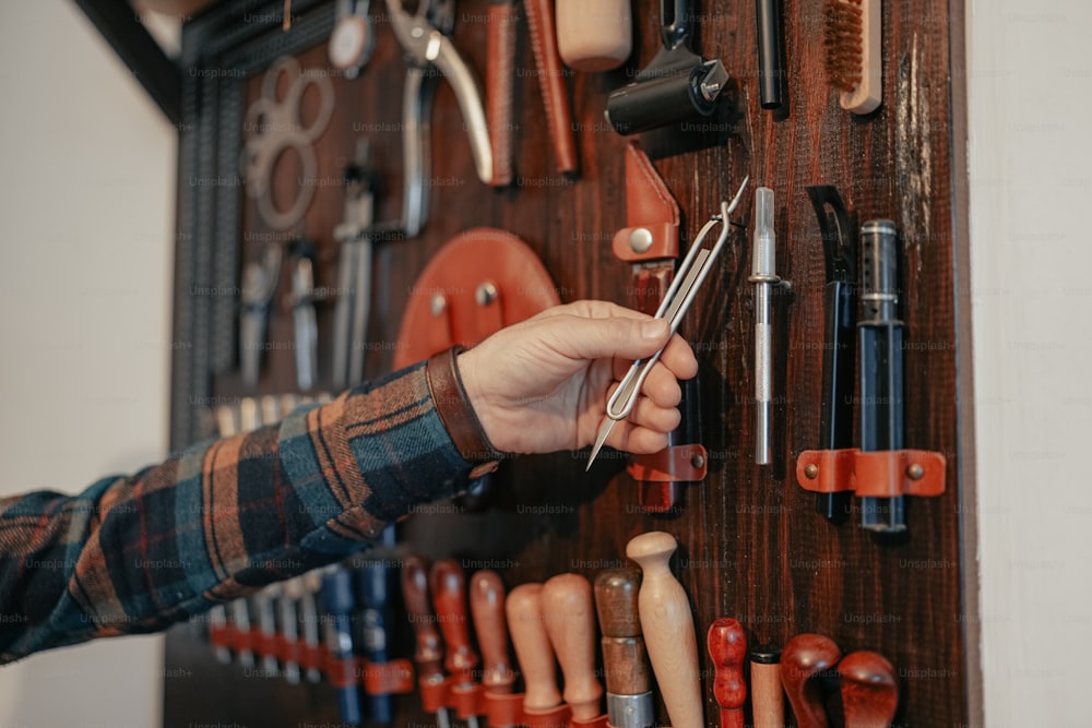 Una persona sosteniendo un par de tijeras frente a una pared de herramientas