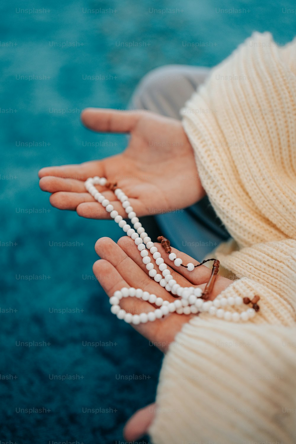 a woman wearing a white sweater and pearls on her hands