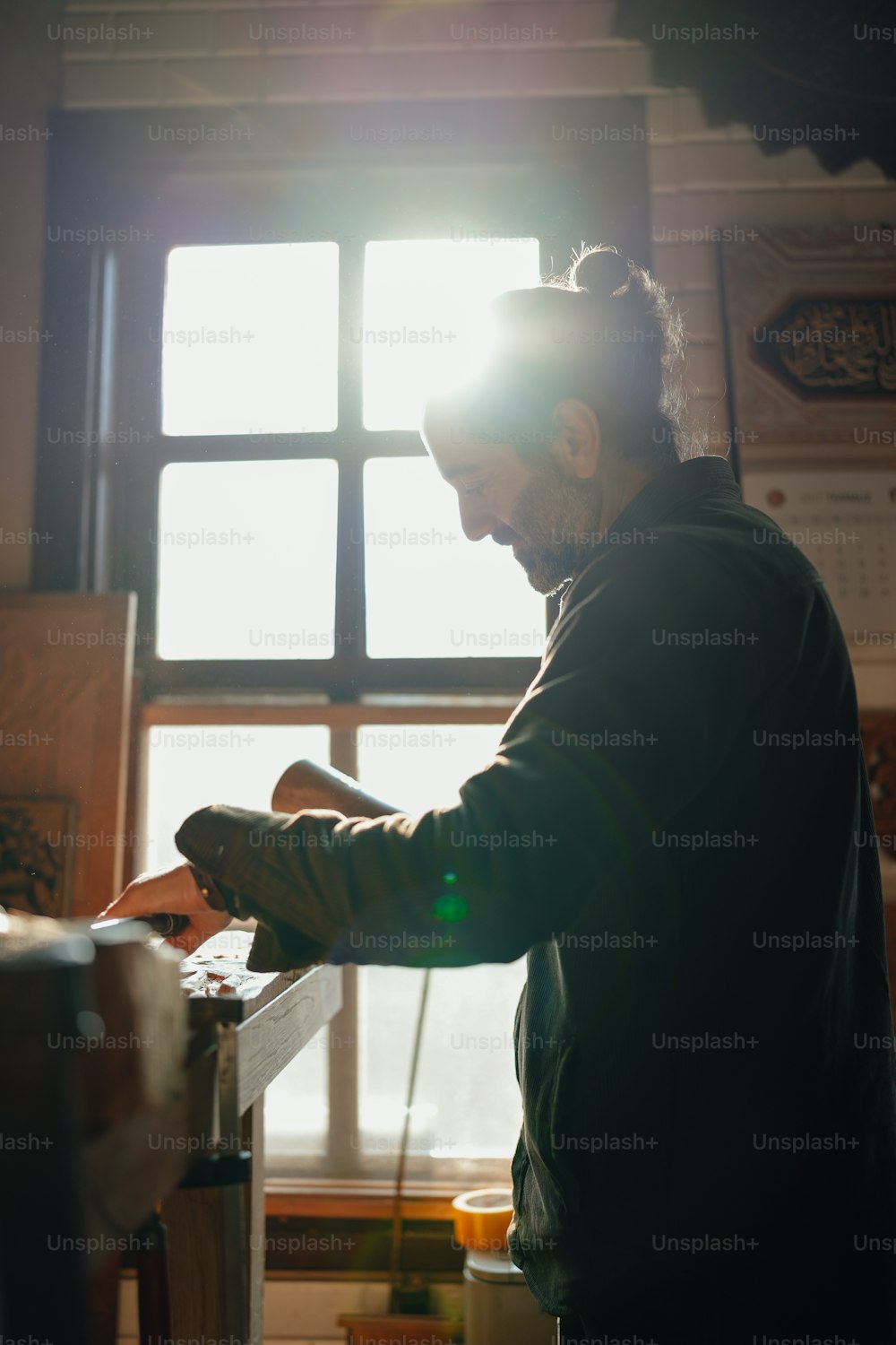 a man standing in front of a window working on a piece of wood