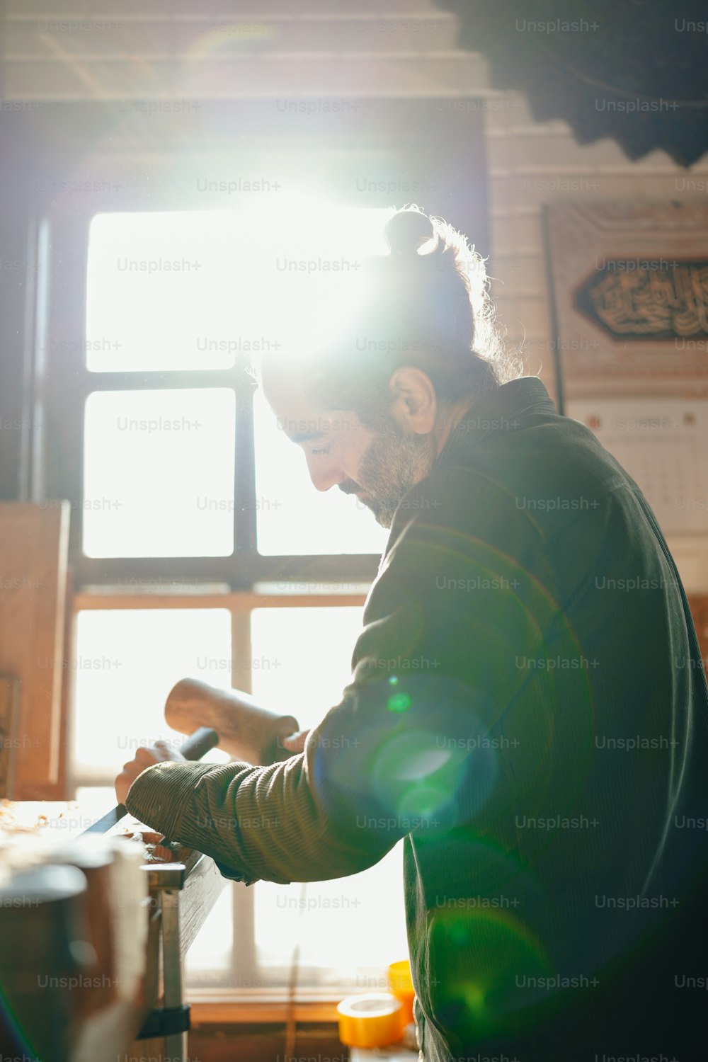 Ein Mann steht vor einem Fenster und arbeitet an einem Stück Holz